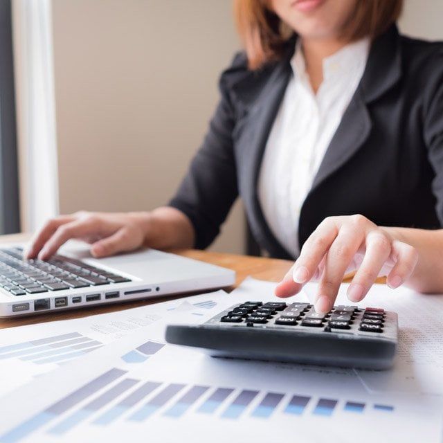 Person using a laptop and calculator with financial documents on a desk ( USA Cabinets Outlet )