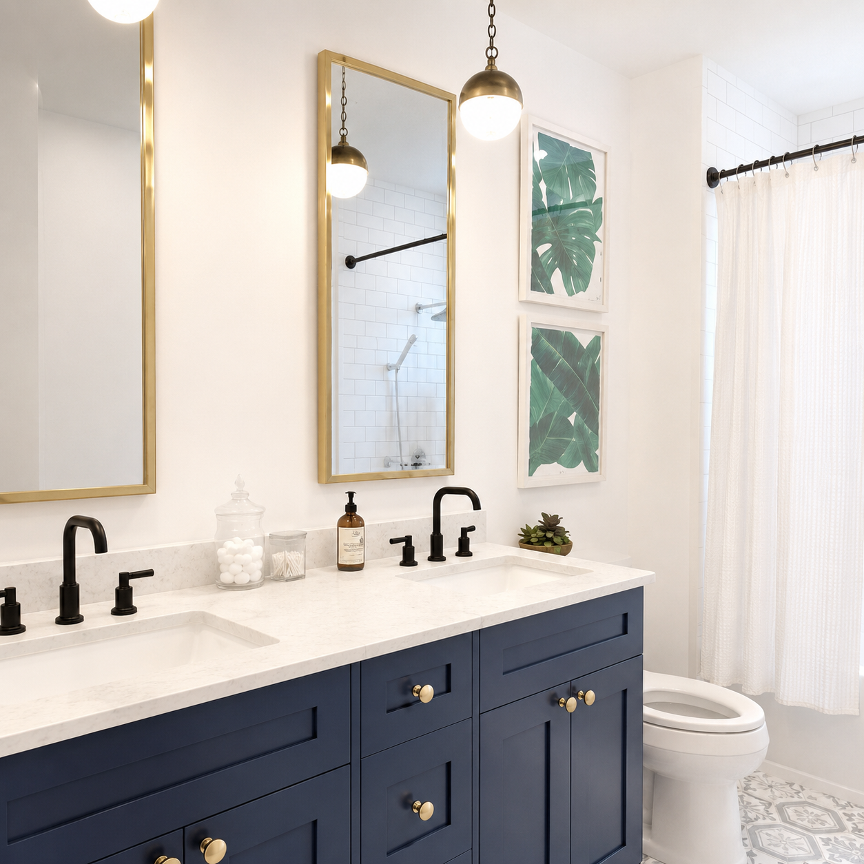 A modern bathroom vanity featuring a navy blue cabinet with gold hardware, a white double-sink countertop, black faucets, and gold-framed mirrors. The room is styled with green botanical wall art, pendant lights, and a white toilet next to a white shower curtain.|USA Cabinets Outlet |