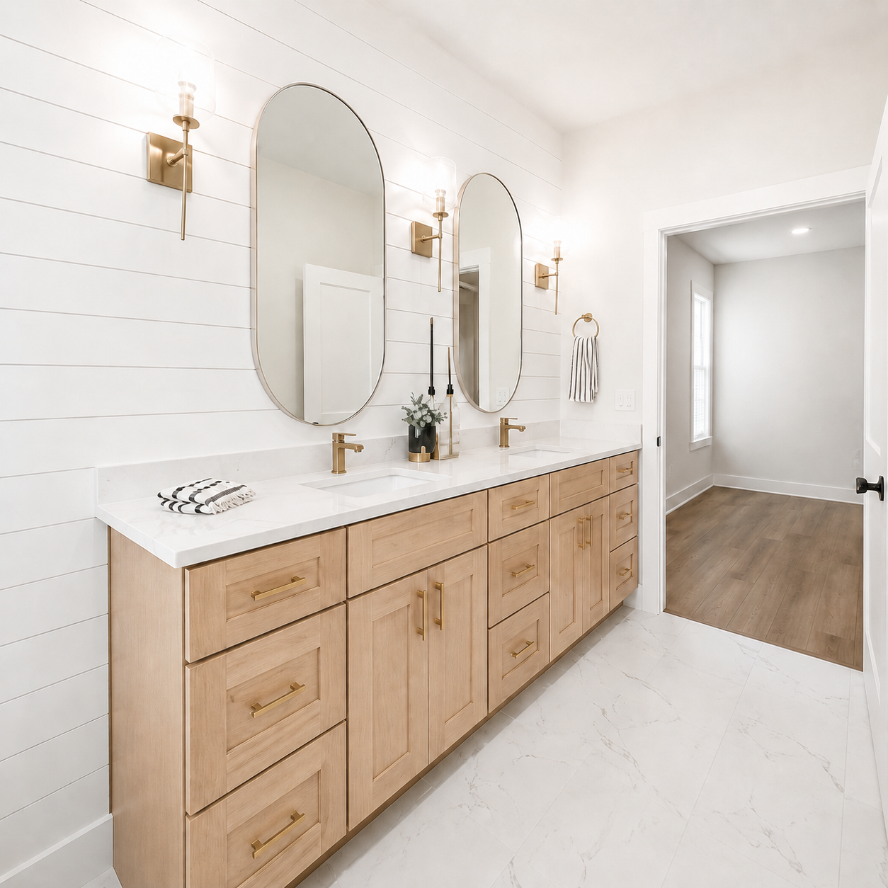 A modern double bathroom vanity with light oak wood cabinets, white marble countertops, two large oval mirrors, and gold wall sconces in a bright white shiplap bathroom.|USA Cabinets Outlet |